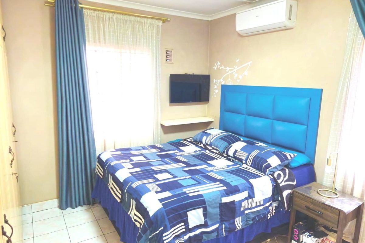 A functional bedroom featuring tiled flooring, a wall-mounted air conditioning unit, and built-in shelving, providing a comfortable and practical living space.
