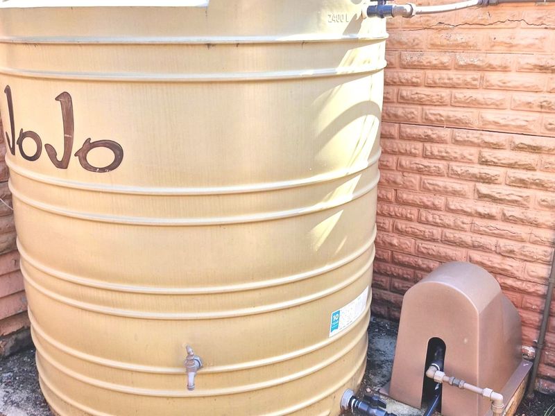 A 2400L water storage tank with an integrated pump system, installed on a concrete base against a brick wall.