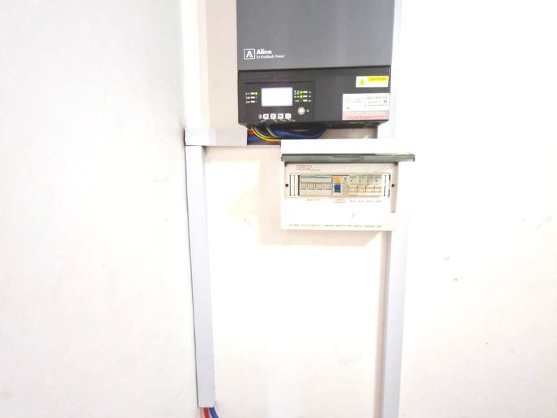 Wall-mounted solar inverter and electrical distribution board with visible conduit and circuit breakers.