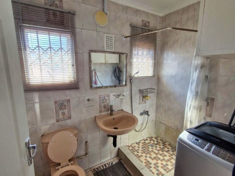 A compact bathroom featuring dated peach-colored sanitaryware, a raised shower area, and tiled finishes, offering potential for a modern renovation.