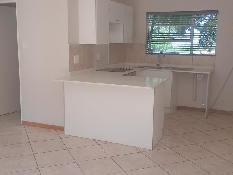 Open plan kitchen area featuring white cabinetry, tiled flooring, and a breakfast counter, presented in a clean, vacant condition.