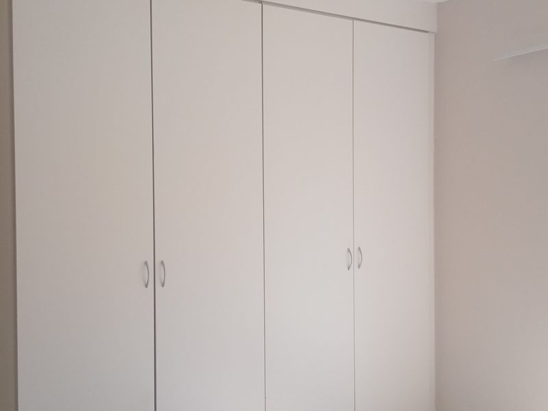 A clean, empty bedroom featuring neutral walls, built-in cupboards, and a window overlooking the exterior area.