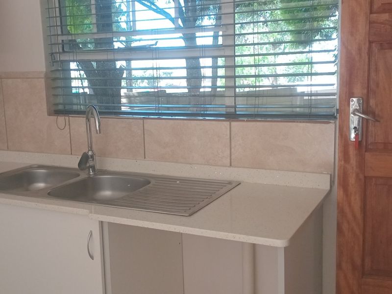 A clean kitchen area featuring a double bowl stainless steel sink, stone countertops, tiled splashback, and a solid wooden door.