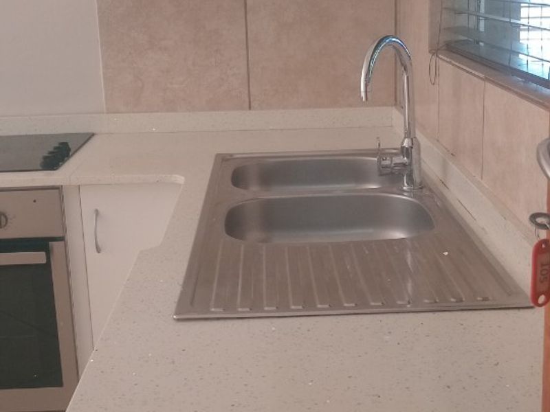 A clean, functional kitchen featuring stone countertops, stainless steel sink, built-in oven, and hob with neutral tiled finishes.