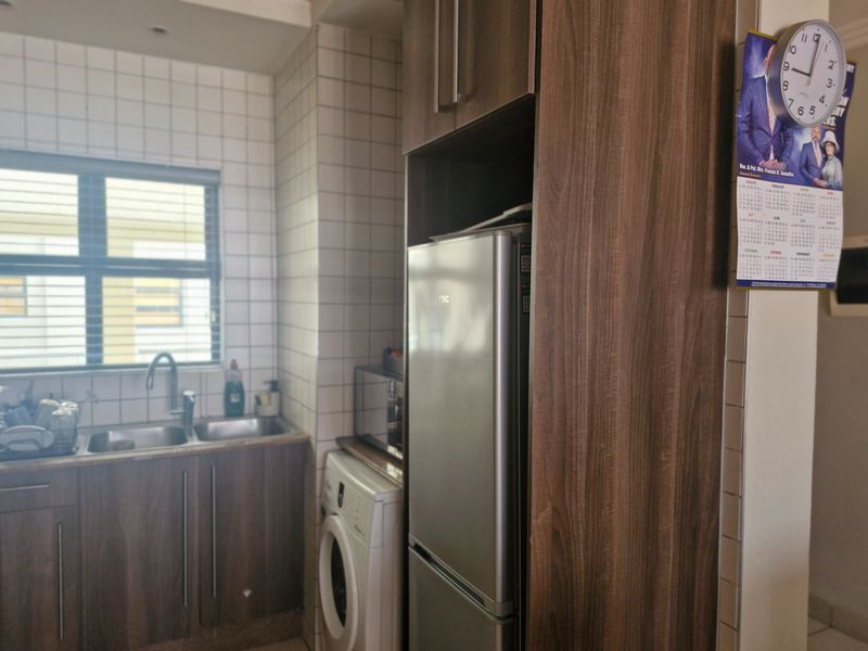 A functional kitchen area featuring wood-finish cabinetry, a double sink with tiled backsplash, and integrated space for laundry and refrigeration appliances.