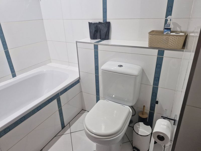 A functional bathroom featuring a white bathtub, a standard toilet, and white wall tiles with decorative blue accent strips.