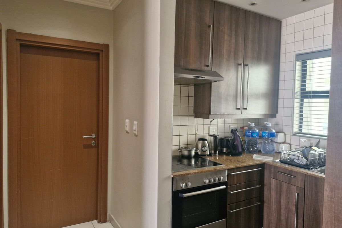 Compact kitchen featuring dark wood cabinetry, granite countertops, built-in oven and stove, and a tiled backsplash with a window for natural light.