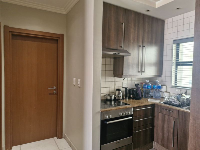 Compact kitchen featuring dark wood cabinetry, granite countertops, built-in oven and stove, and a tiled backsplash with a window for natural light.