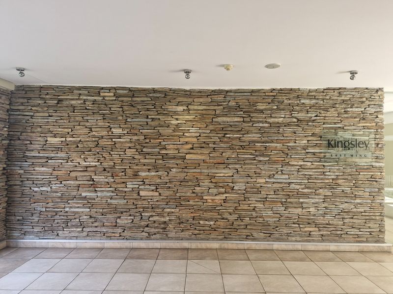 A clean and modern building entrance lobby featuring a prominent natural stone feature wall and neutral floor tiling.