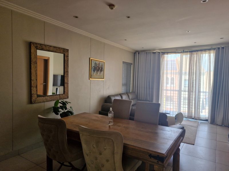 An open-plan living and dining area featuring tiled flooring, recessed lighting, and large sliding doors leading to a balcony with natural light.