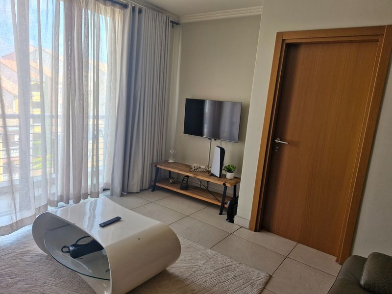 A bright living room featuring tiled flooring and a large sliding glass door providing access to a balcony.