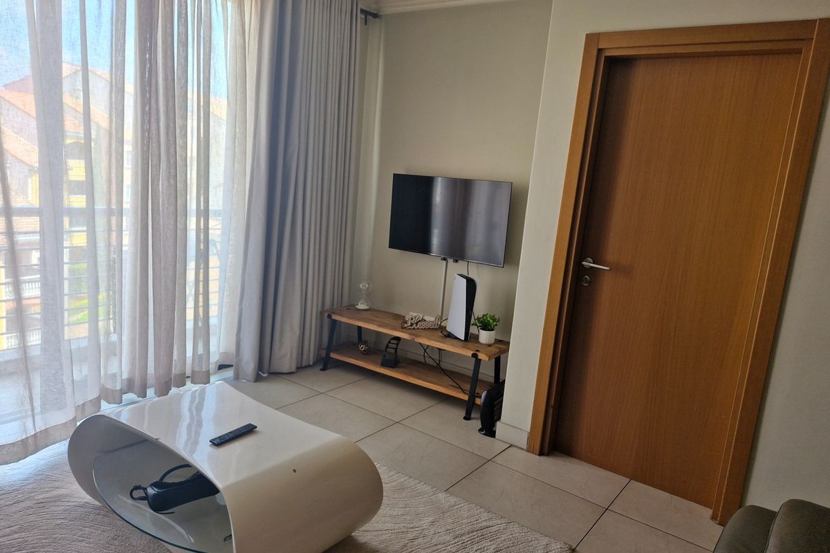 A bright living room featuring tiled flooring and a large sliding glass door providing access to a balcony.