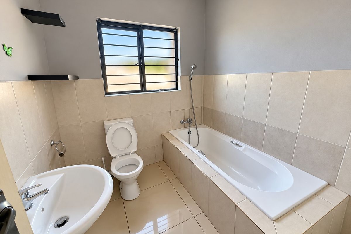 A clean, modern bathroom featuring a pedestal basin, a built-in bathtub with a handheld shower mixer, and neutral wall and floor tiling.