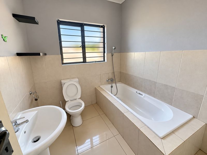 A clean, modern bathroom featuring a pedestal basin, a built-in bathtub with a handheld shower mixer, and neutral wall and floor tiling.