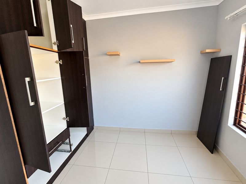 A bedroom featuring tiled flooring, built-in dark wood cupboards, and floating wall shelves. The room is vacant and ready for personalization.