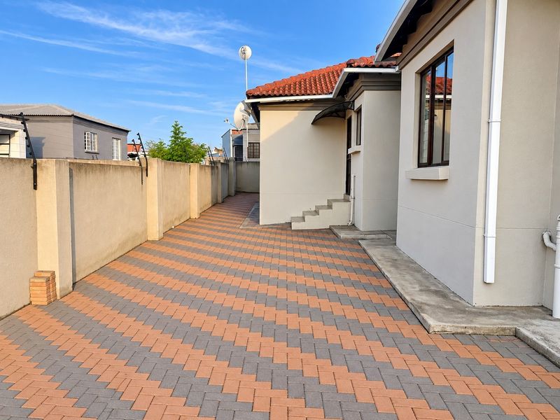 A well-maintained rear exterior area featuring patterned brick paving, a secure perimeter wall with electric fencing, and concrete steps leading to the house.