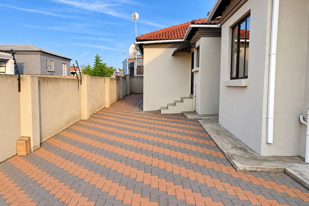 A well-maintained rear exterior area featuring patterned brick paving, a secure perimeter wall with electric fencing, and concrete steps leading to the house.