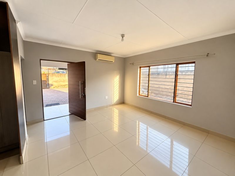 A bright, empty bedroom featuring tiled flooring, a built-in cupboard, an air conditioning unit, and a secure window with security bars.