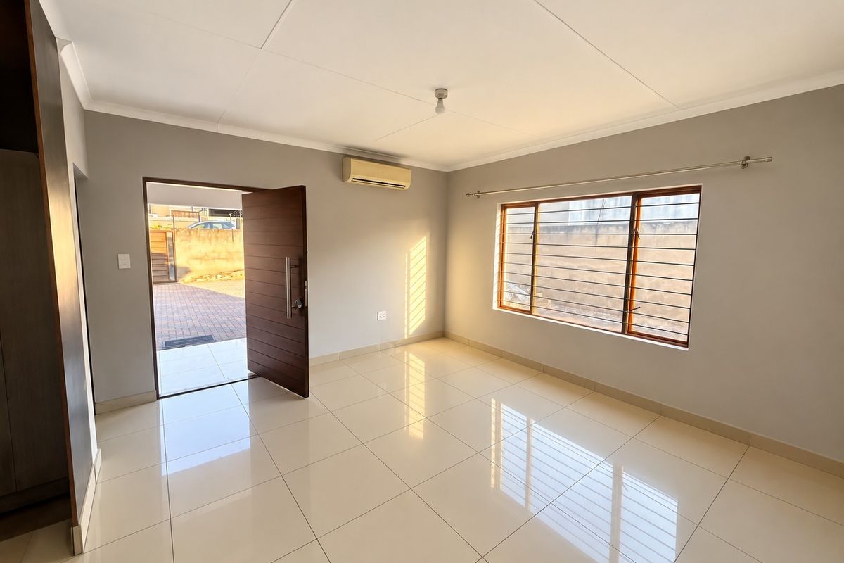 A bright, empty bedroom featuring tiled flooring, a built-in cupboard, an air conditioning unit, and a secure window with security bars.