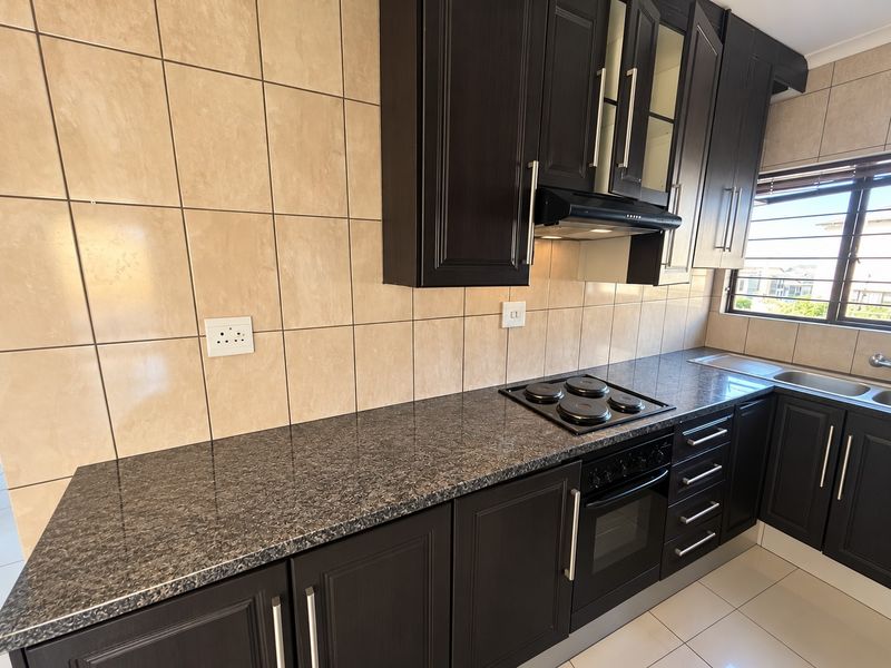 A well-maintained kitchen featuring dark wood cabinetry, granite countertops, a built-in oven with electric hob, and a tiled backsplash.