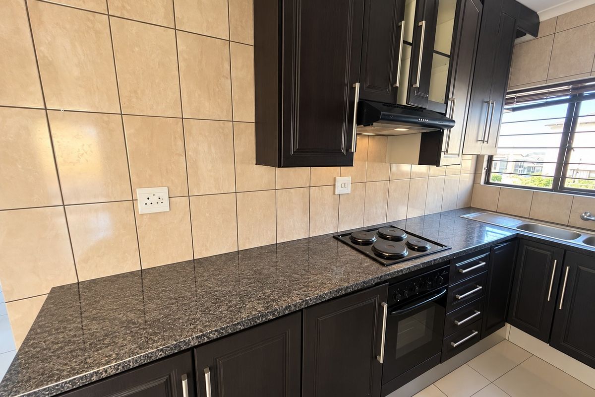 A well-maintained kitchen featuring dark wood cabinetry, granite countertops, a built-in oven with electric hob, and a tiled backsplash.