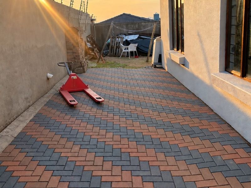 A paved rear patio area featuring a herringbone pattern, enclosed by a perimeter wall with electric fencing and modern aluminium window frames.