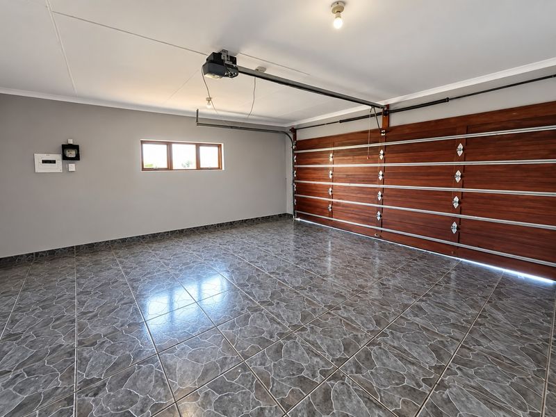 A clean, spacious double garage featuring tiled flooring, a wooden sectional garage door, and an automated door motor.