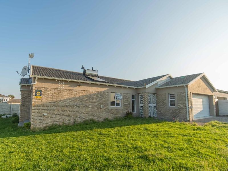 Rear view of a single-story brick house featuring a solar water heater, security gate, and an attached garage with a paved driveway.