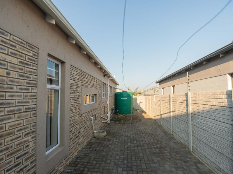Side exterior view of the property featuring a paved walkway, brick facade, and a water storage tank enclosed by a precast concrete boundary wall.