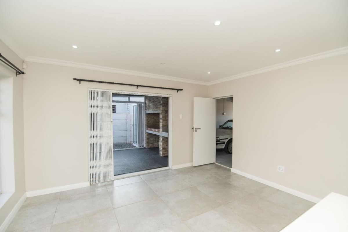 Spacious living area featuring neutral tiled flooring, recessed lighting, and direct access to an outdoor patio area with a built-in braai.
