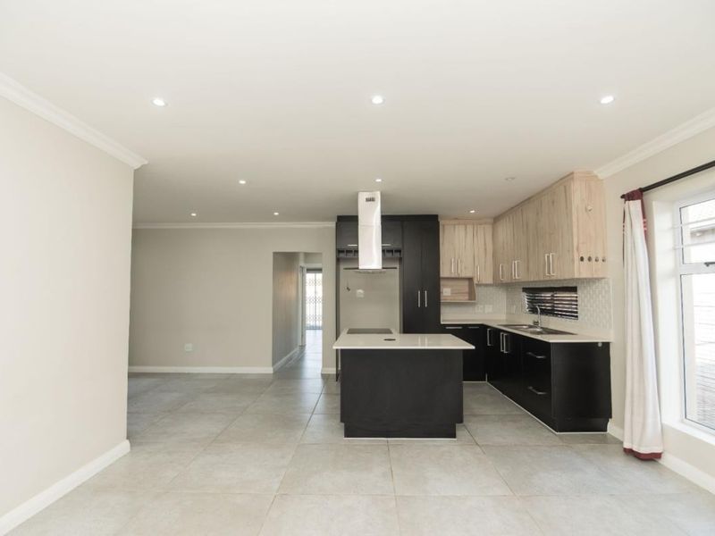 Modern open-plan kitchen featuring a central island, sleek cabinetry, tiled flooring, and recessed lighting, offering a clean and functional space.