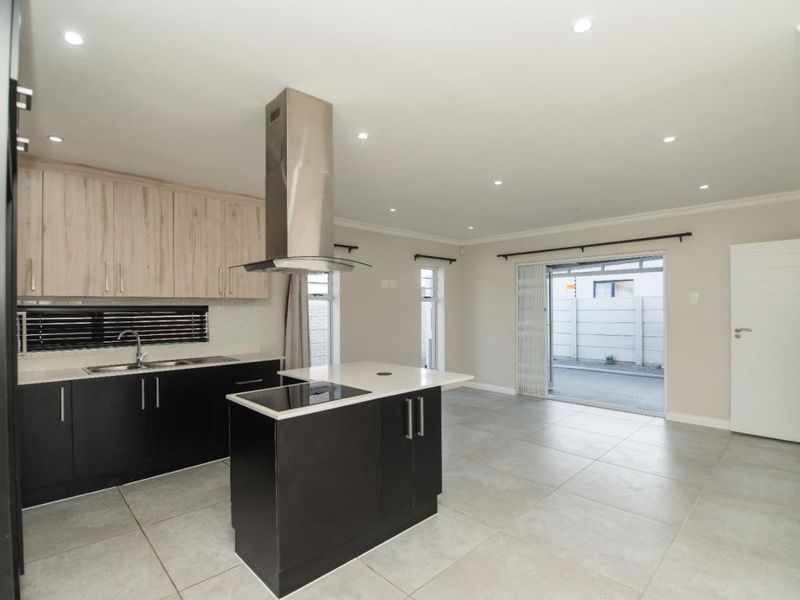 Modern open-plan kitchen and living area featuring sleek cabinetry, a central island with hob, tiled floors, and direct access to the patio.