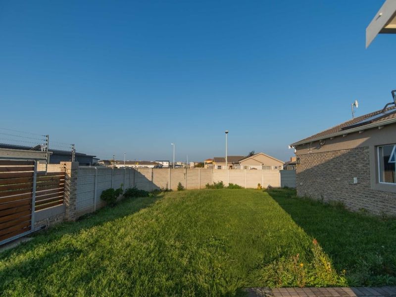 A spacious rear garden featuring a well-maintained lawn, enclosed by a precast concrete boundary wall and a timber gate, adjacent to the main dwelling.