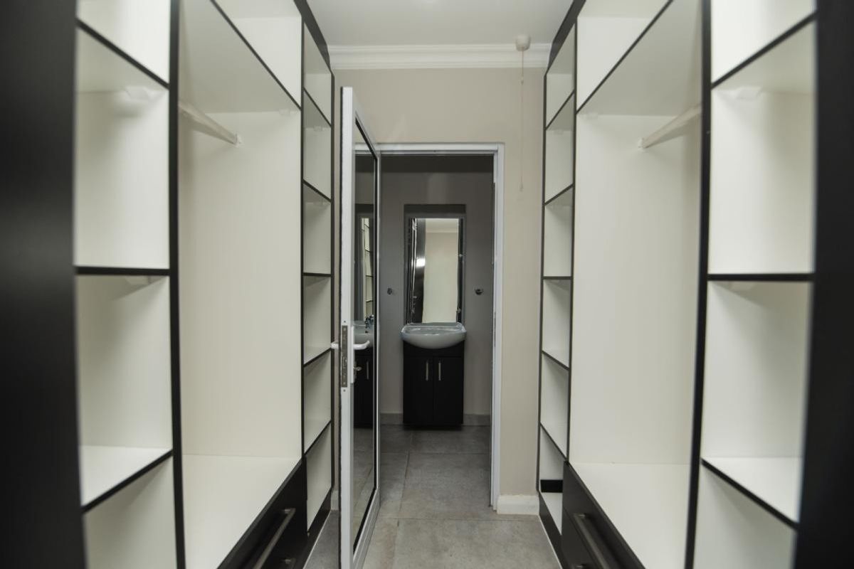 A walk-in dressing area featuring extensive built-in cabinetry with modern shelving, leading directly into an en-suite bathroom with a vanity basin.
