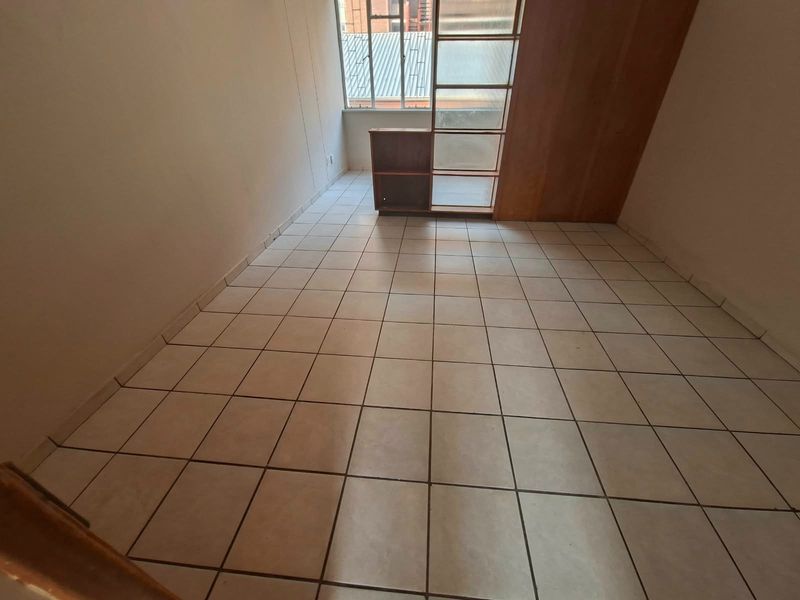 An empty bedroom featuring tiled flooring and a built-in wooden shelving unit, offering a blank canvas for potential renovation or staging.