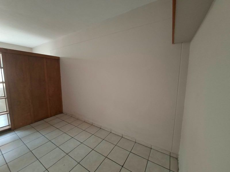 An empty bedroom featuring ceramic tile flooring and a built-in wooden wardrobe, offering a blank canvas for personalization.