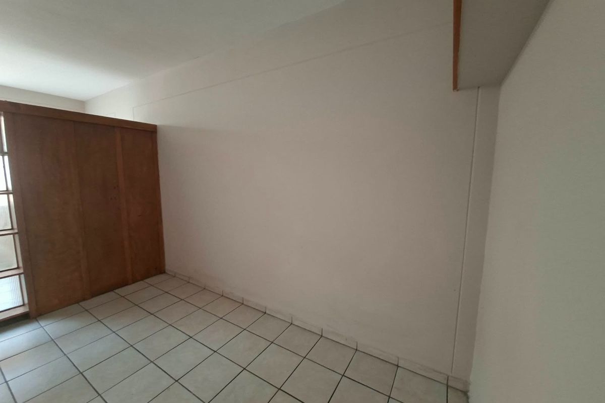 An empty bedroom featuring ceramic tile flooring and a built-in wooden wardrobe, offering a blank canvas for personalization.