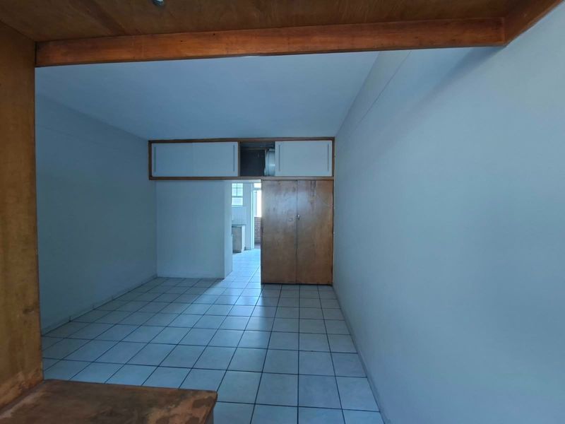 An empty living area featuring tiled flooring, built-in wooden cupboards with overhead storage, and an exposed timber beam, offering a blank canvas for renovation.