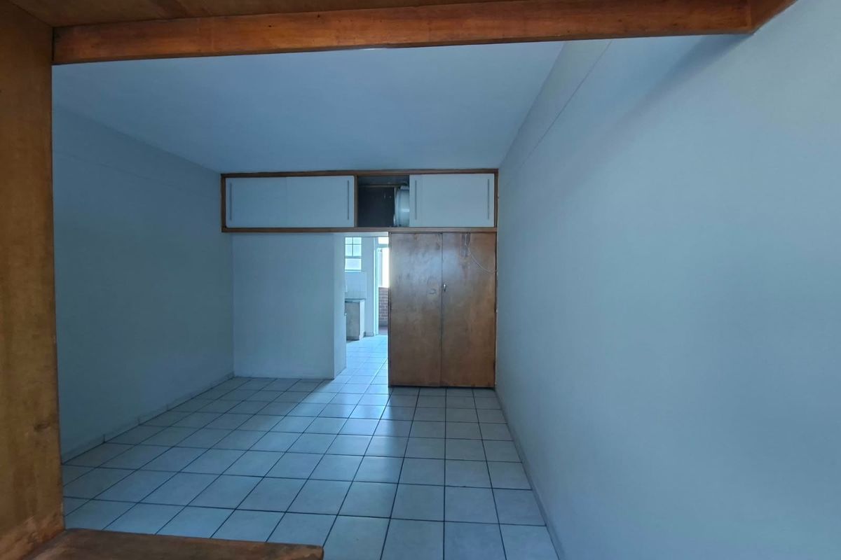 An empty living area featuring tiled flooring, built-in wooden cupboards with overhead storage, and an exposed timber beam, offering a blank canvas for renovation.