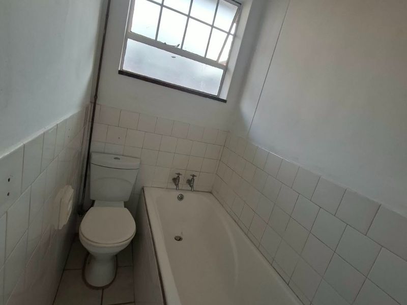 A compact bathroom featuring a standard bathtub, toilet, and tiled finishes, currently in need of cosmetic updates and maintenance.
