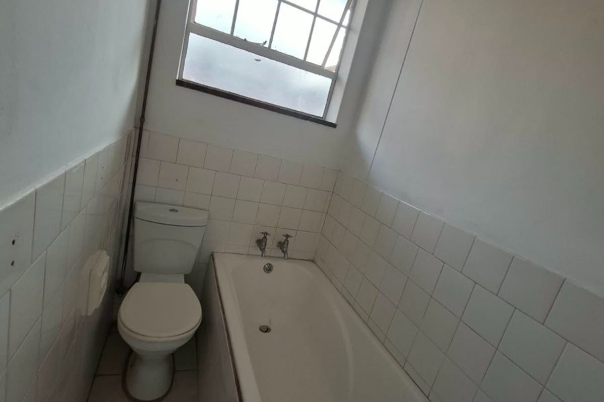 A compact bathroom featuring a standard bathtub, toilet, and tiled finishes, currently in need of cosmetic updates and maintenance.
