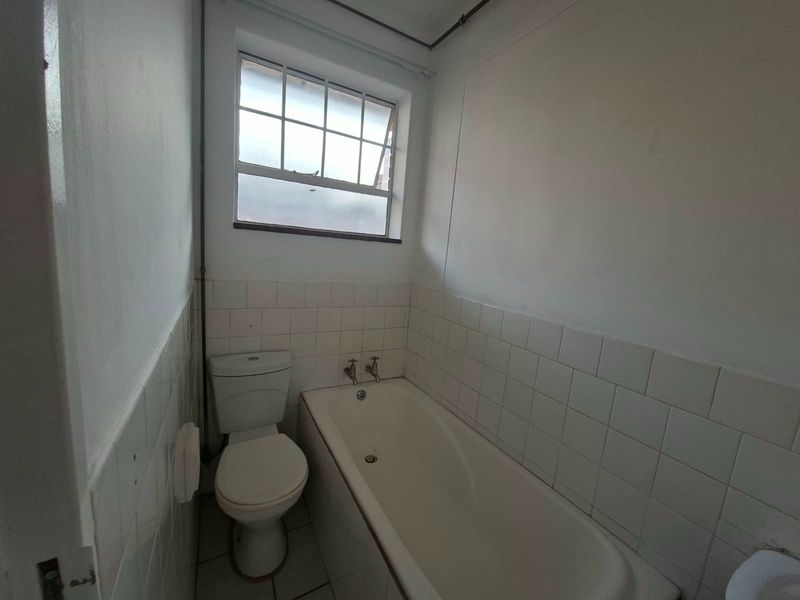 A dated bathroom featuring a standard bathtub, toilet, and tiled finishes, requiring cosmetic updates to improve its overall condition and appeal.