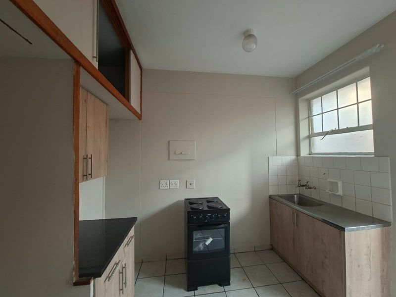 A compact, empty kitchen featuring built-in cabinetry, a stainless steel sink, tiled splashback, and a freestanding electric stove.