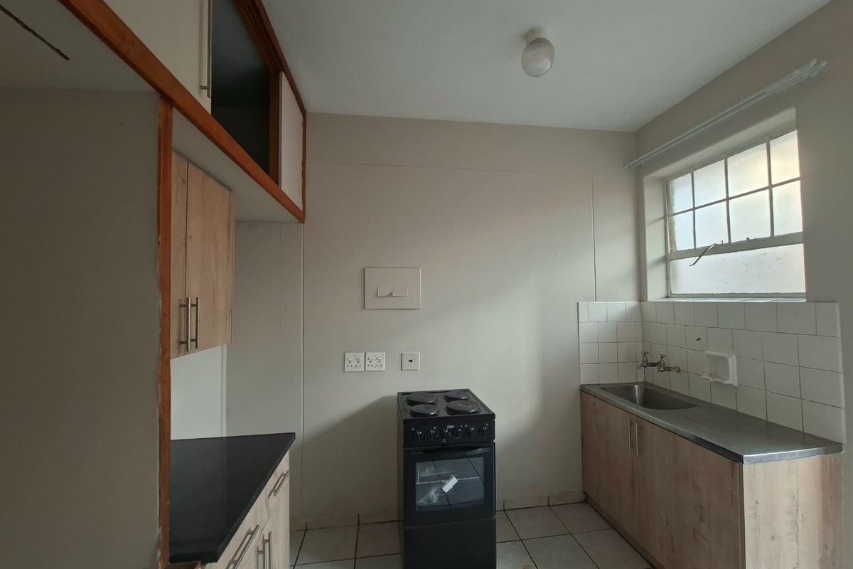 A compact, empty kitchen featuring built-in cabinetry, a stainless steel sink, tiled splashback, and a freestanding electric stove.