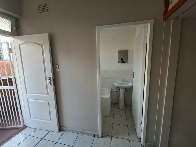 A compact bathroom featuring a pedestal basin and built-in bathtub with tiled flooring and wall finishes, requiring cosmetic updates.