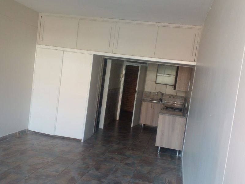 Open plan living area featuring tiled flooring, extensive built-in storage cupboards, and a compact kitchen area with fitted cabinetry and sink.