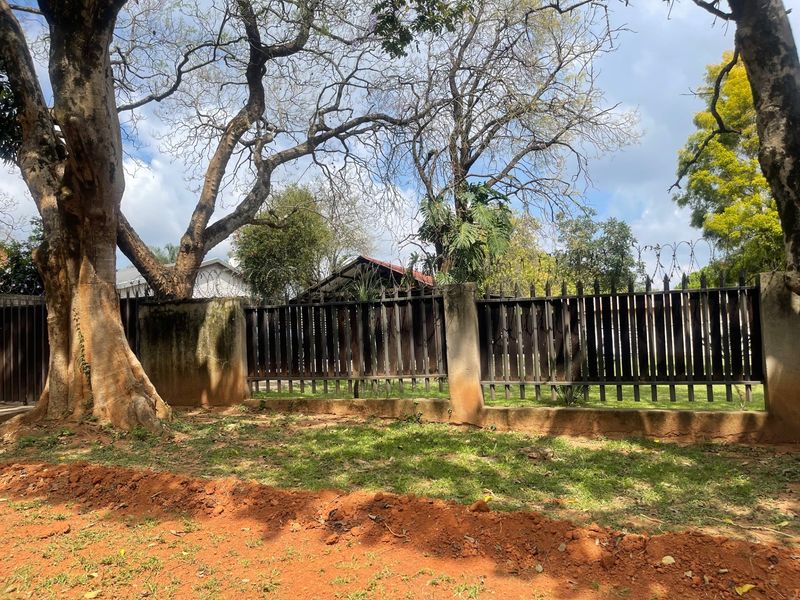 A view of the rear property boundary featuring a metal fence with concrete pillars, topped with security razor wire and surrounded by mature trees.