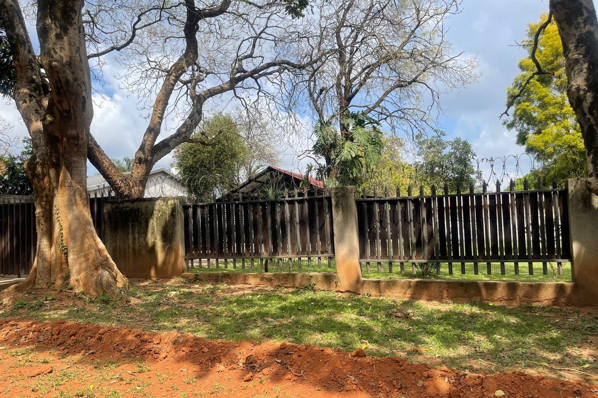 A view of the rear property boundary featuring a metal fence with concrete pillars, topped with security razor wire and surrounded by mature trees.