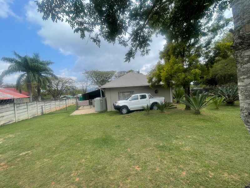 A spacious rear garden featuring a large lawn, paved patio area, water storage tank, and secure boundary walling surrounding the property.