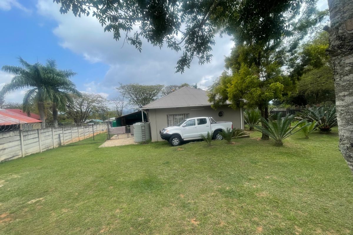 A spacious rear garden featuring a large lawn, paved patio area, water storage tank, and secure boundary walling surrounding the property.